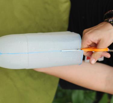 A close up of a milk carton bottle and a hand using scissors to cut up the side of the carton